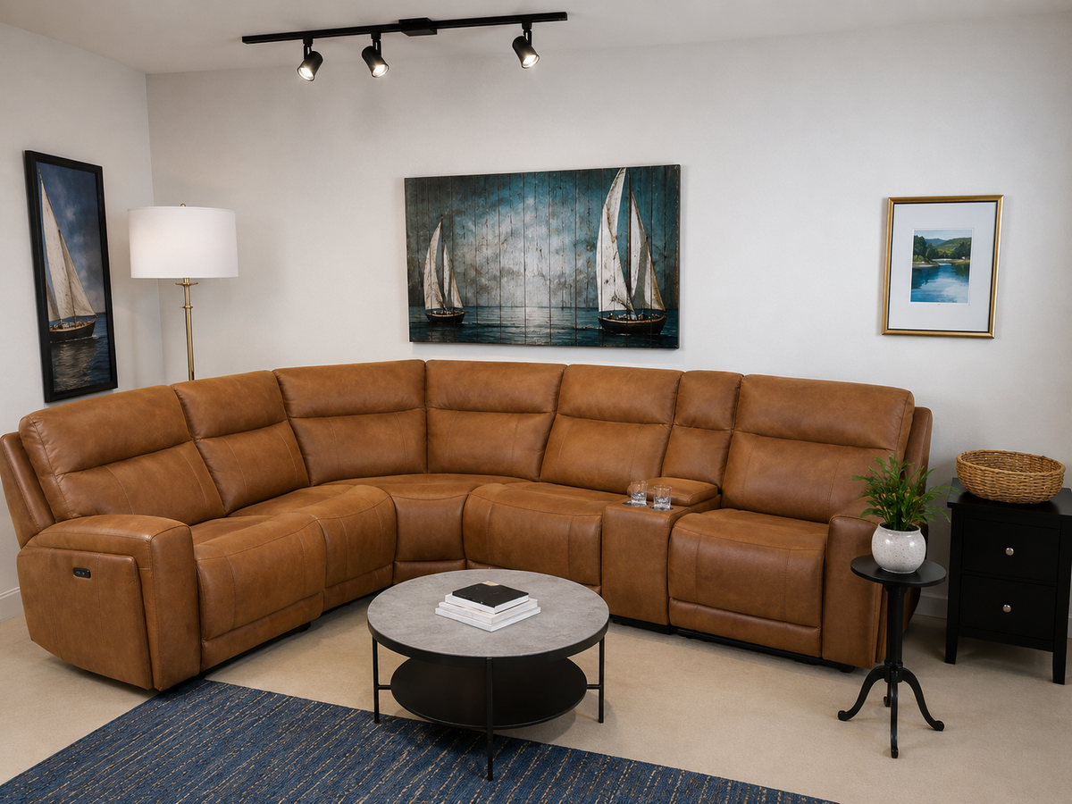 A large U-shaped sectional sofa upholstered in warm tan leather, styled in a modern living room setting with a round coffee table, side table, lamp, and wall art.