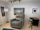 A gray leather recliner chair in a styled room setting with a floor lamp, wall art, a side table, and a plant.