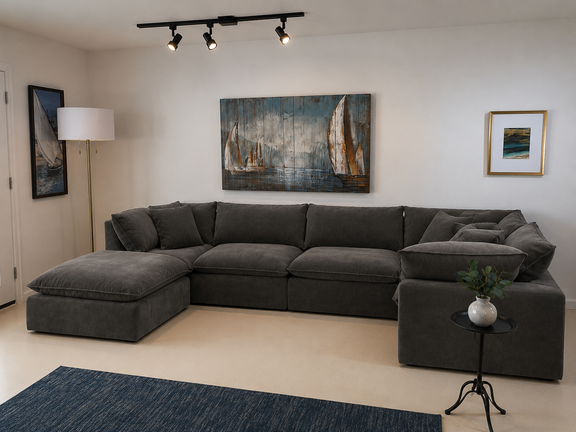 A dark gray sectional sofa with a chaise lounge in a modern living room setting, featuring a blue rug, a small side table with a plant, a floor lamp, and sailboat wall art.