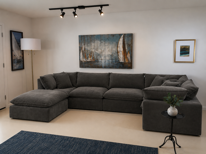 A dark gray sectional sofa with a chaise lounge in a modern living room setting, featuring a blue rug, a small side table with a plant, a floor lamp, and sailboat wall art.